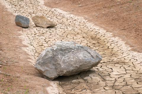 Three stones lying in a dried up and cracked river bed.